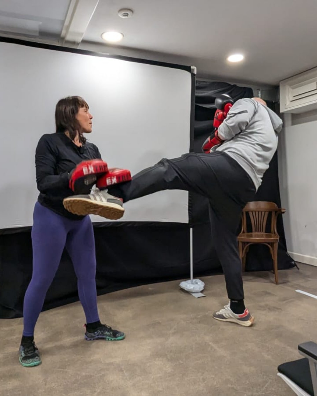A trainer holding pads for a client's high kick